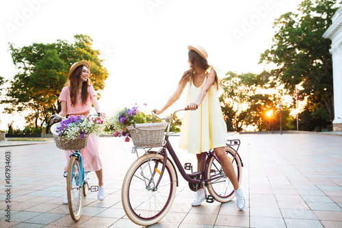 Two young pretty women in dresses sitting on retro bicycles