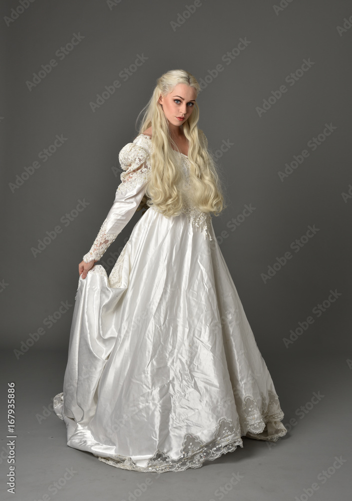 full length portrait of a beautiful blonde woman wearing link white gown, standing pose against a grey background. full length portrait of a beautiful blonde woman wearing link white gown, standing pose against a grey background.