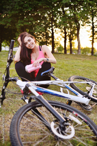 Pretty girl with a bike on a bike ride with a bottle of water or a protein cocktail on the background of nature