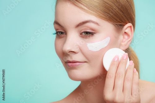 Woman removing makeup with cream and cotton pad