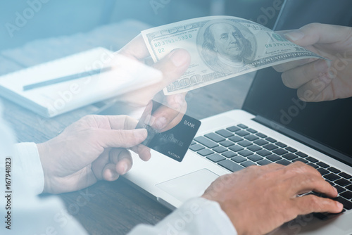 Hands holding credit card and using laptop double exposure with hands holding cash us dollar..Man shopping online at restaurant online business concept..