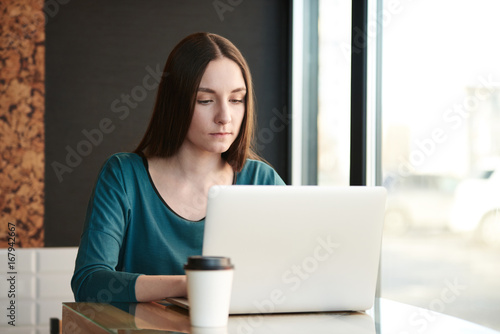 Young woman working on laptop while sitting at cafe