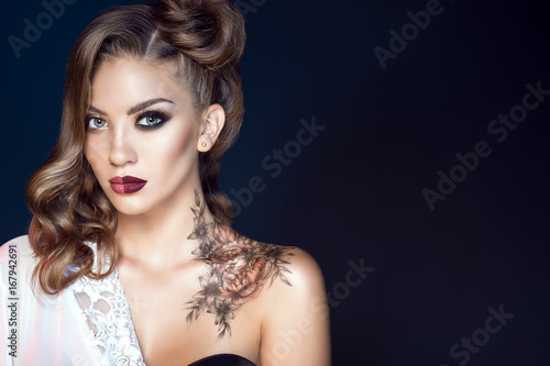 Close up portrait of glam model with artistic make up and hairstyle. Body art on her shoulder. Ideal woman concept. One half symbolizes a good housewife, another one – a passionate lover. Copy-space photo