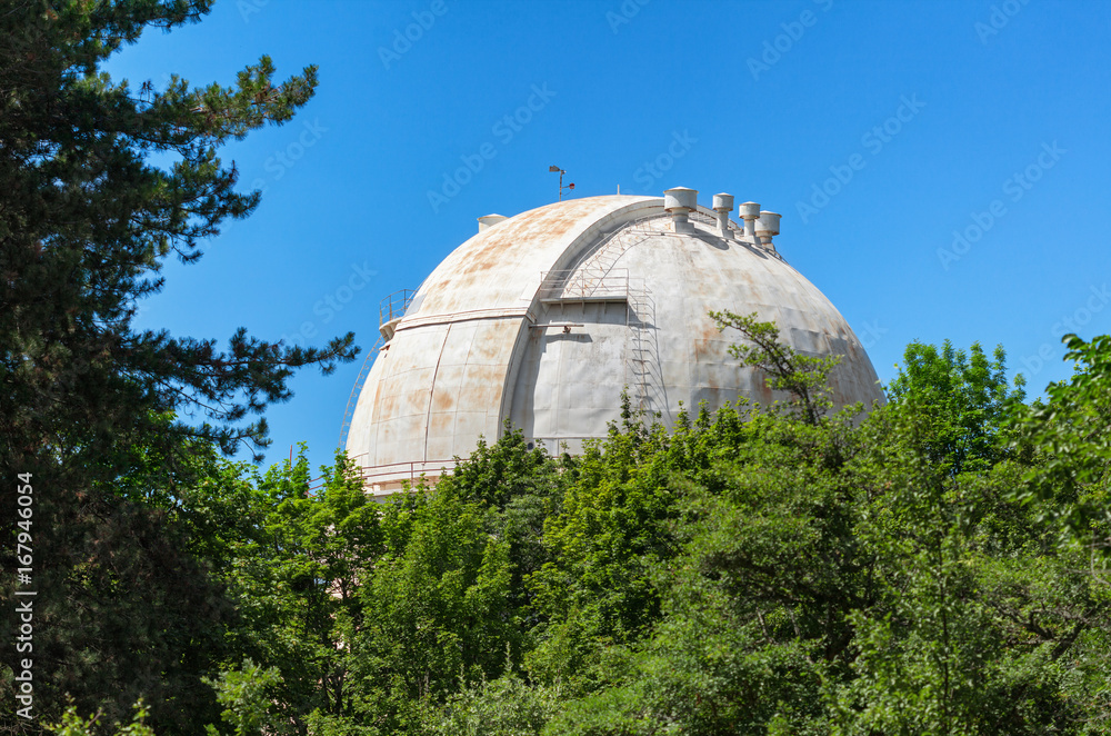 Giant white dome of the reflecting telescope covered with rust at the Observatory among the trees