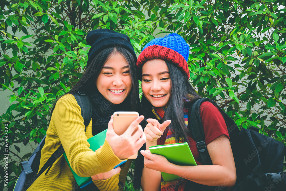 Two young asian travelers who are wearing colorful clothes with beanies and scarves are searching the information or checking the location on the phone