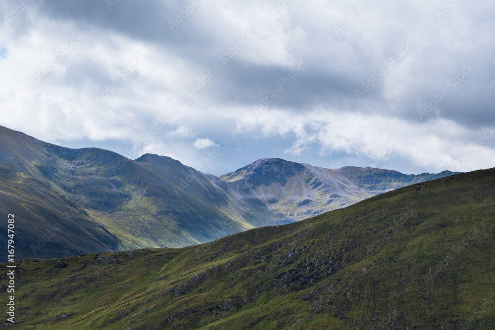 Scottish Highland hillsides in shifting colours against cloudy sky background Scottish Highland hillsides in shifting colours against cloudy sky background