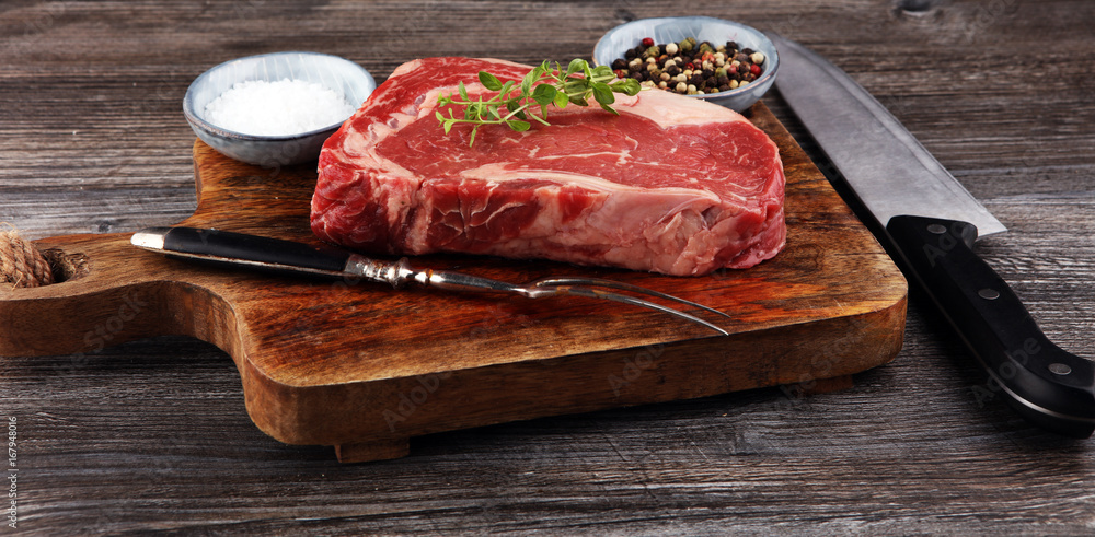 Raw fresh meat Ribeye Steak, seasoning and meat fork on dark background Raw fresh meat Ribeye Steak, seasoning and meat fork on dark background