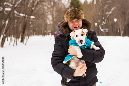 Pet owner, dog, and people concept - Young smiling caucasian man holding Jack Russell terrier outdoor in winter time.