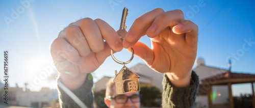 Property, ownership, new home and people concept. Cheerful young man holding house key. photo