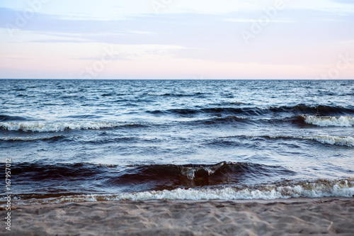 North seascape on Lake Onega - waves beat against the granite shore which reflects the rays of the setting sun.