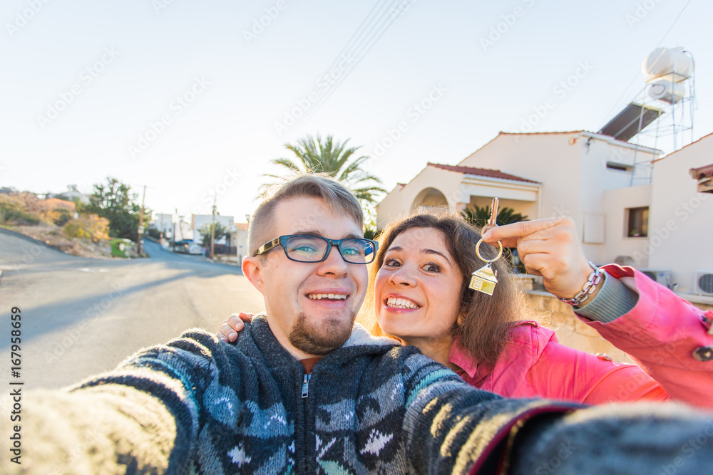 Funny couple With Keys Standing Outside New Home. Real estate, owner and people concept