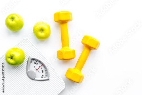 Sport and diet for losing weight. Bathroom scale, apple and dumbbell on white background top view copyspace