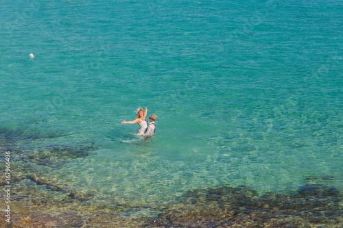 Romantic newly-married couple enjoying a summer vacation. Young groom lifting his bride in sea.