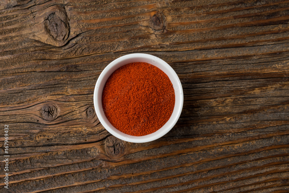 Paprika powder in white bowl on an old wooden table Paprika powder in white bowl on an old wooden table