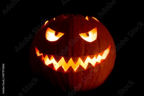 Round halloween pumpkin smile with hot burning fire eyes mouth. The big helloween symbol has a mad face glowing eyes and also a glow in its mouth and teeth. Black orange nightmare of October 31st