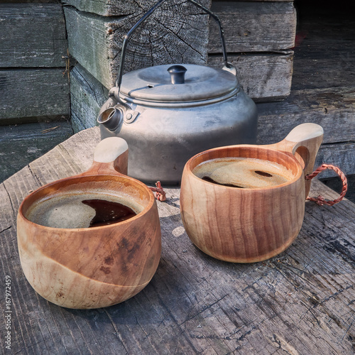 Two wooden mugs filled with hot fresh coffee on the campsite while trekking. © Teemu Tretjakov