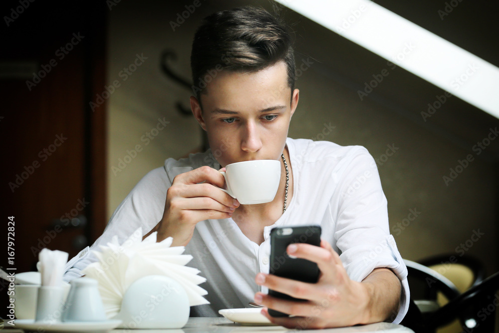Young man with mobile drinks coffees in a cafe Young man with mobile drinks coffees in a cafe