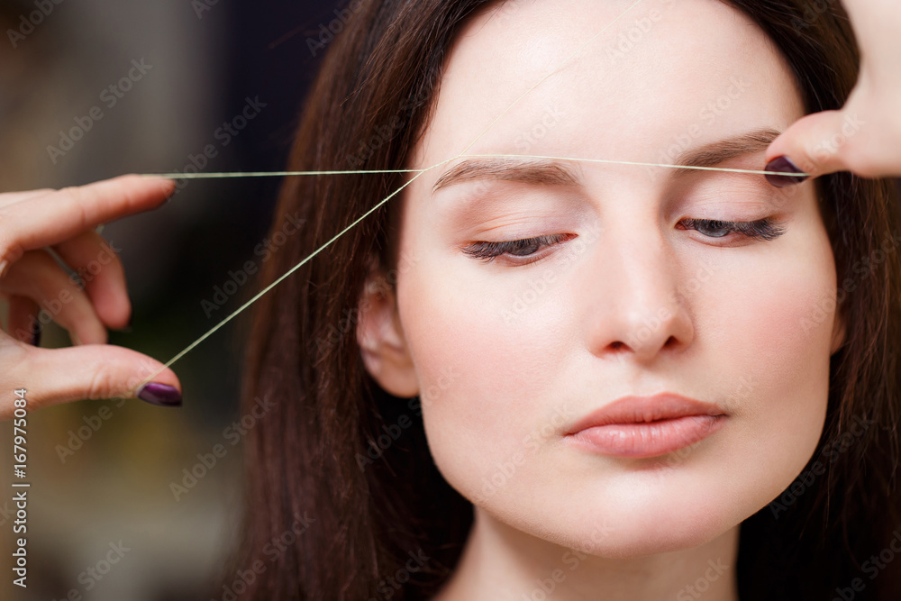Cosmetologist plucks client eyebrows by thread Cosmetologist plucks client eyebrows by thread