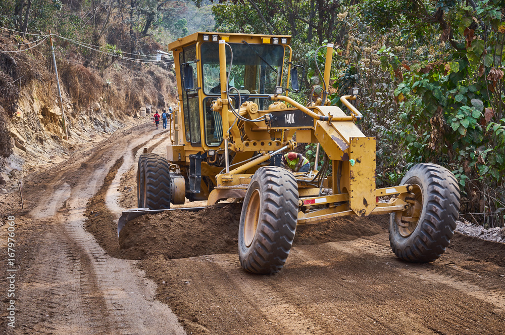 Heavy machine on road construction in Guatemala / Grader pushing dirt to level the dirt road 
