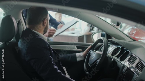 Stylish businessman signs the conract of buying auto in car dealership photo