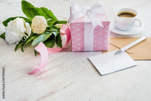 Obraz na płótnie Pink dotted gift box, empty greeting card, kraft envelope, peonies bouquet and coffee cup over white wooden rustic table. Romantic holiday and event concept. w salonie