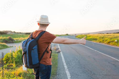 Man with Backpacks in casual Travel Clothes walking along road ,Road hitch-hiking. Traveler standing at the highway hitching