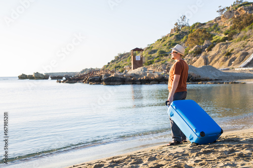 Man in sunglasses with luggage on the sea in summer sunny day