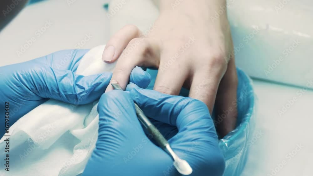 Manicurist in blue rubber gloves in salon using scalpel to cut cuticle off client fingers, close up Manicurist in blue rubber gloves in salon using scalpel to cut cuticle off client fingers, close up