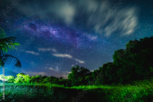 Blue night starry sky above countryside and Green field.  Night view of natural Milky Way glowing stars.