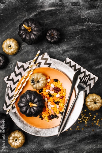 Halloween Table setting on dark background. Dish with sweets  on a dark table with black and gold pumpkin. Flat lay, top view trendy holiday concept.