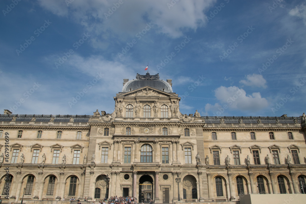 Inner courtyard and exterior of The Louvre Museum with walking tourists in a summer day