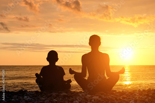 Mom and son meditate on the beach in lotus position. Silhouettes  sunset