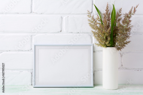 White landscape frame mockup with grass and green leaves in cylinder vase