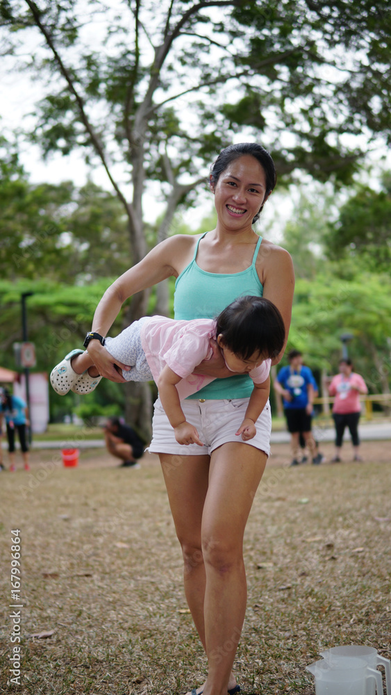 Asian woman carrying toddler and participating in family games outdoor