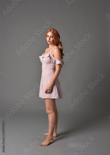 full length portrait of pr a pretty girl wearing simple purple dress, standing pose against a grey background © faestock
