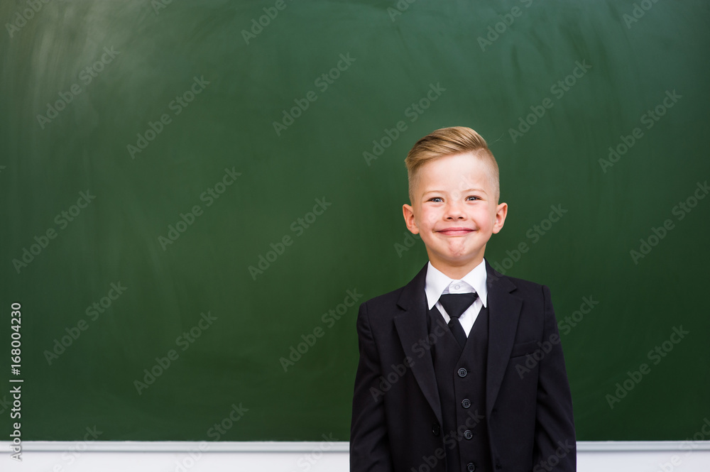 Smiling boy in a suit standing near empty green chalkboard Smiling boy in a suit standing near empty green chalkboard