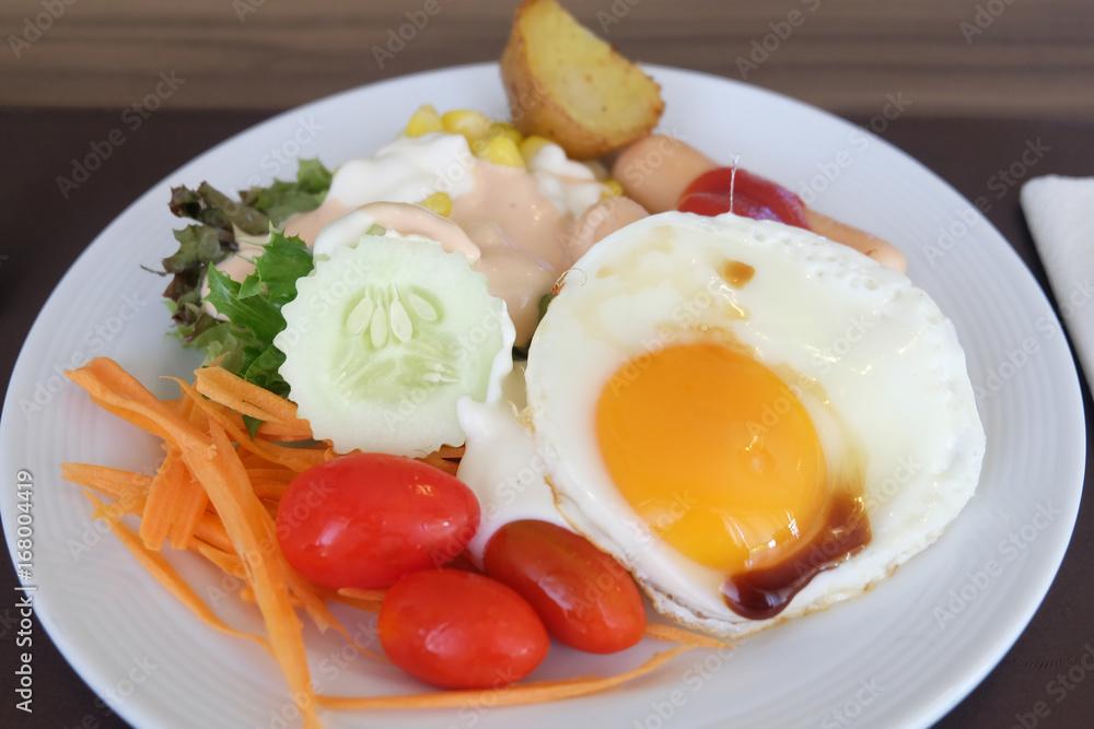 Salad vegetables, sausage, fried eggs in a white plate on the table Salad vegetables, sausage, fried eggs in a white plate on the table