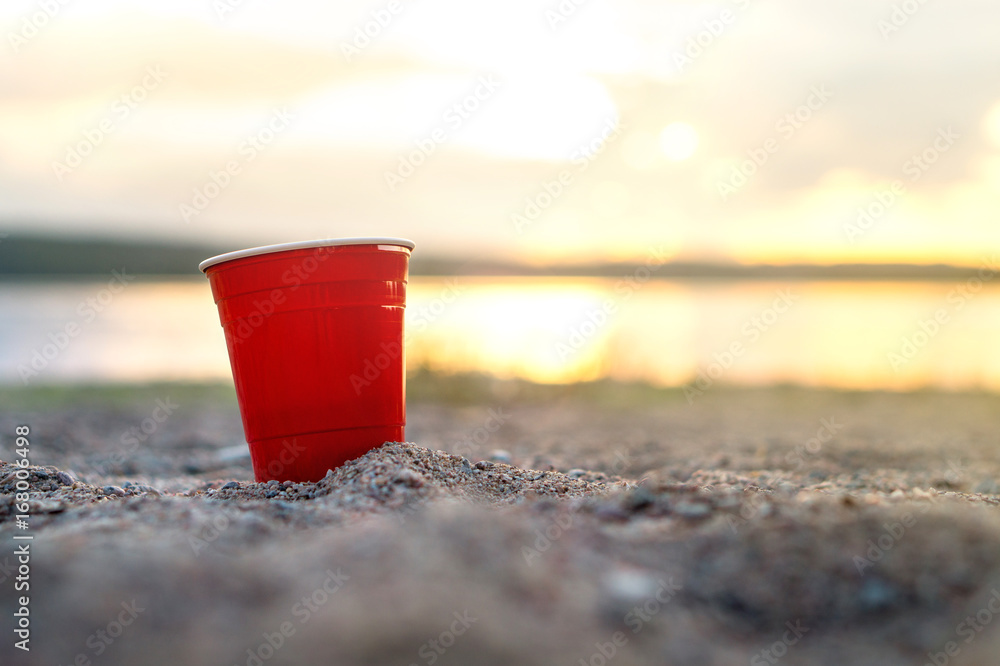 Red party cup in sand at sunset. Summer beach party concept with copy space. Red party cup in sand at sunset. Summer beach party concept with copy space.