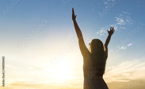 Brave happy young woman raising hands up in the air and open arms to sky. Enjoying life. Sunny healthy lifestyle concept in sunset.