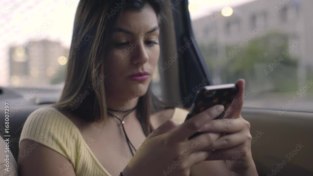 Friends Use A Rideshare, Closeup Of Hispanic Young Woman Using Her Smartphone In Back Seat Of Moving Car Friends Use A Rideshare, Closeup Of Hispanic Young Woman Using Her Smartphone In Back Seat Of Moving Car