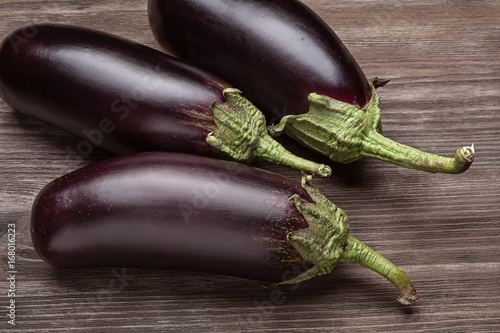 Fotografie Three fresh eggplants on a wooden surface.