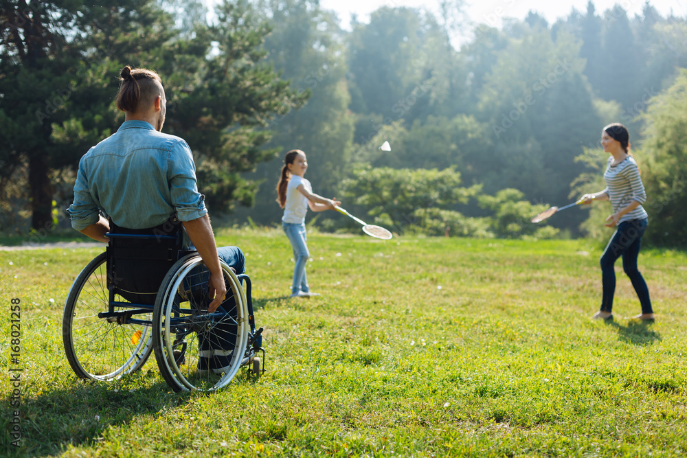 Young man in wheelchair watching his family play badminton Young man in wheelchair watching his family play badminton