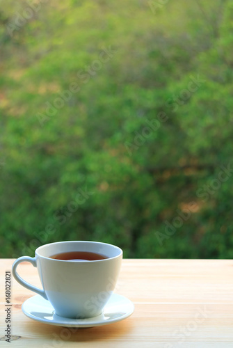 One Cup of Hot Tea Served on Wooden Table by the Window, with Blurred Background of Big Green Tree 