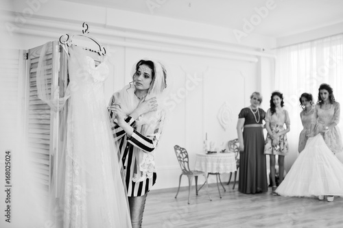 Bridesmaids and mother looking at bride while she is dressing up. Black and white photo.