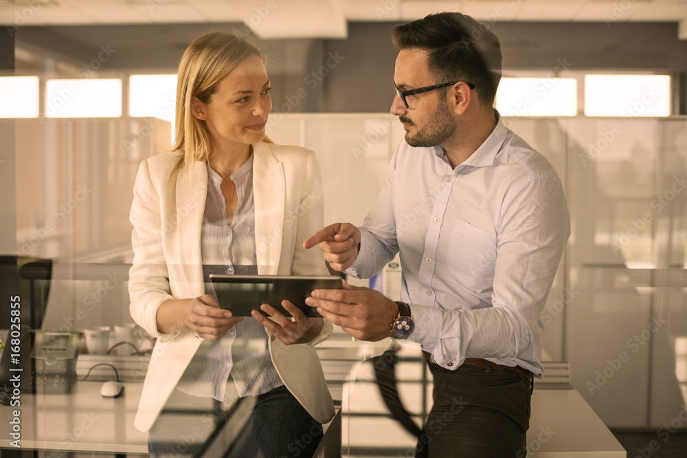Business people standing in office. Business woman showing something to her colleague on digital tablet. Business people standing in office. Business woman showing something to her colleague on digital tablet.