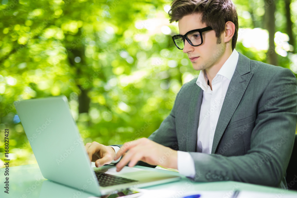 Young handsome manager working at laptop at office table in green park. Business concept. Young handsome manager working at laptop at office table in green park. Business concept.