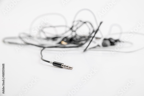 Black and white tangled little headphones lie on a white isolated background. Horizontal frame