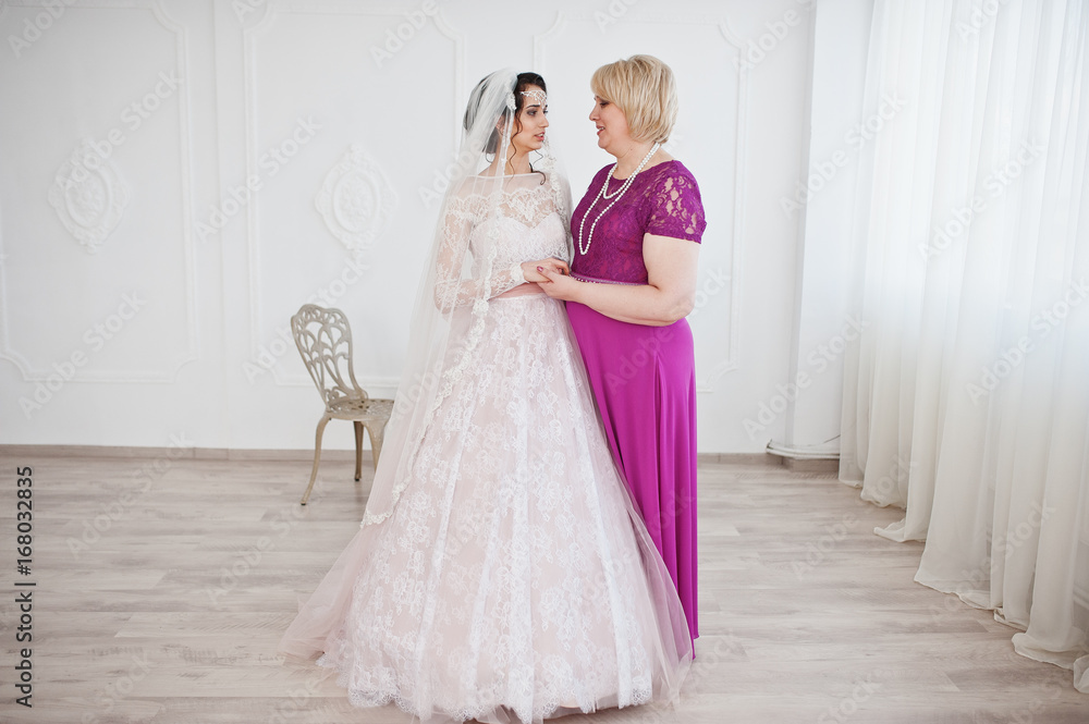 Lovely bride in wedding gown posing with her mother in purple long dress. Lovely bride in wedding gown posing with her mother in purple long dress.
