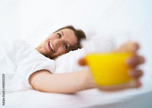 Cute girl sleeping in bed waking up stretching, smiling and drinks orange juice in bed in the morning