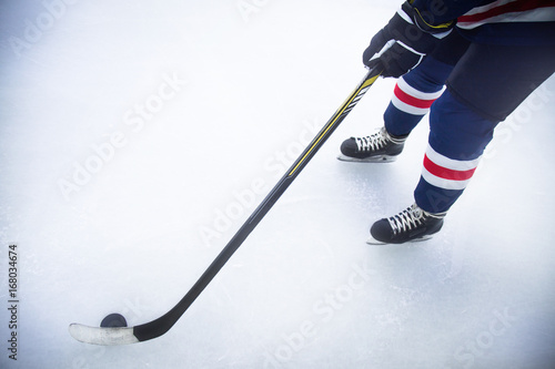 Photography the legs of a hockey player skating on ice with stick and puck close up